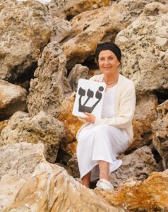 Picture of Marcella Levie, in a desert setting, holding the Hebrew letter Shin