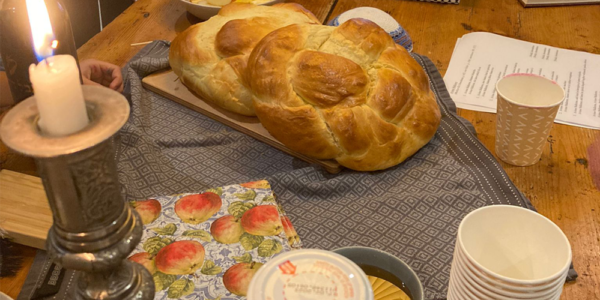 Challah, apple, honey and lit kiddush candles on a table