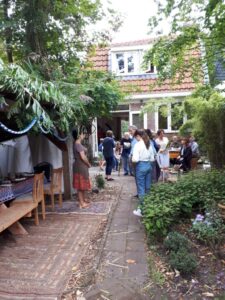 People gathering in a garden of a home, with a laden table, happily chatting and mingling on a bright day